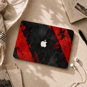 May include: A rectangular laptop skin featuring a bold, abstract design with diagonal stripes of vibrant red and deep black, characterized by a distressed, paint-splatter texture. The center displays a white Apple logo cutout.
