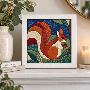 May include: A square framed wall art piece featuring a stylized fabric-textured illustration of a squirrel holding an acorn. The squirrel has a large, multi-colored tail with orange, red, and cream patterns, set against a dark blue and green background.