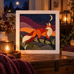 May include: A square framed fabric art piece featuring a stylized red fox standing in a landscape at night. The scene includes a crescent moon, rolling hills in shades of purple and orange, and textured green ground, all enclosed in a light wood frame.