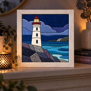 May include: A square framed wall art piece featuring a stained glass style illustration of a white lighthouse with a red top. The scene depicts a dark blue night sky with clouds, a rocky coastline, and blue ocean waves in a segmented design.