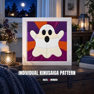 Könnte beinhalten: Ein quadratisches, gerahmtes Kinusaiga-Kunstwerk mit einem weißen Geist mit schwarzen Augen und Mund vor einem Hintergrund aus violetten, orangefarbenen und gepunkteten violetten Stoffsegmenten. Darunter steht der Text INDIVIDUAL KINUSAIGA PATTERN und HAZEL & WONDER.
