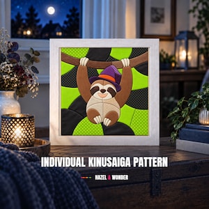 Può includere: Un'opera d'arte Kinusaiga incorniciata di forma quadrata raffigurante un bradipo sorridente che indossa un cappello da strega viola con una fascia arancione, appeso a un ramo marrone. Lo sfondo presenta un motivo geometrico di tessuto verde brillante, nero e a pois.