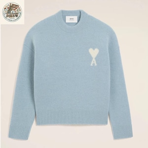 Può includere: Un maglione a maniche lunghe color azzurro con girocollo, polsini e orlo a coste. Il capo presenta un logo bianco ricamato a forma di cuore con la lettera A sul lato sinistro del petto. Un'etichetta bianca interna sul collo riporta il marchio ami.