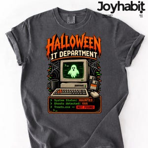 May include: A charcoal grey t-shirt featuring a graphic of a vintage computer with a glowing green ghost on the screen. The text reads HALLOWEEN IT DEPARTMENT, System Status: HAUNTED, Ghosts detected: 666, and Treats.exe - NOT FOUND.