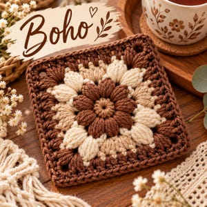 Può includere: Un sottobicchiere quadrato all'uncinetto con un motivo floreale centrale a punto nocciolina nei toni del marrone scuro, marrone chiaro e crema. Il design include una sovrapposizione decorativa con il testo Boho e un piccolo cuore.