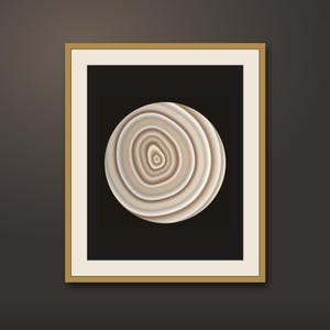 May include: A framed wall art piece featuring a circular, layered agate-style design in shades of beige, cream, and white. The circular graphic is centered on a solid black background, enclosed within a white mat and a thin, metallic gold frame.