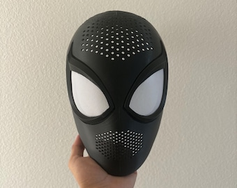 May include: A matte black full-face mask featuring large, almond-shaped white mesh eye lenses. The mask has a perforated texture across the forehead and mouth area, with a smooth, contoured surface design that covers the entire face.