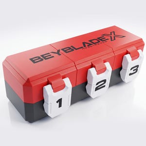 Op de afbeelding: Een rechthoekige opbergkoffer met een rood deksel en een zwarte basis, voorzien van de tekst BEYBLADE X op de bovenkant. De voorzijde heeft drie witte sluitingen met de zwarte cijfers 1, 2 en 3 om de vakken van de kunststof doos te sluiten.