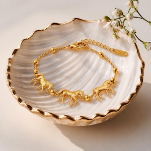May include: A gold-toned chain bracelet featuring three horse charms interspersed with small round beads. The bracelet includes a lobster claw clasp and an adjustable extender chain with a small rectangular tag at the end.