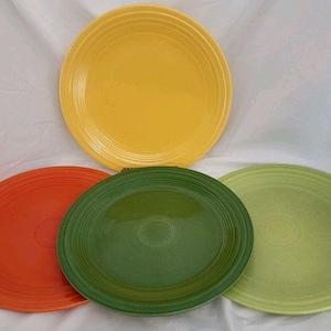May include: A set of four round ceramic dinner plates featuring concentric ring patterns along the rims. The plates are finished in solid glossy glazes of bright yellow, vibrant orange, deep forest green, and a lighter shade of lime green.