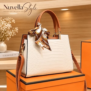May include: A white handbag with a textured crocodile-skin pattern, featuring brown handles and a detachable shoulder strap. A decorative silk scarf with a brown, white, and gold chain print is tied to the handle. The text Nuvella Style is visible.
