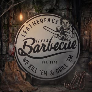 Puede incluir: Un letrero metálico circular con un gráfico en blanco y negro de un personaje sosteniendo una motosierra. El texto dice LEATHERFACE TEXAS Barbecue WE KILL 'EM & GRILL 'EM EST. 1974. El diseño está centrado sobre un fondo gris claro.