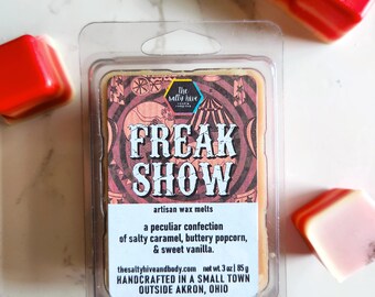 May include: A clear plastic container holding a wax melt. The wax melt is light brown with a red and white design featuring a circus tent and the words "Freak Show". The container text reads "The Sally Hive" and "Artisan Wax Melts". It also includes the text "A peculiar confection of salty caramel, buttery popcorn, & sweet vanilla." and "Handcrafted in a small town outside Akron, Ohio."