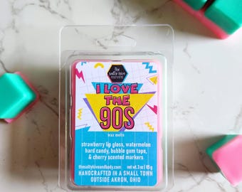 Op de afbeelding: Een roze wax melt met een 90s-thema ontwerp. De wax melt is verpakt in een doorzichtige plastic verpakking. Het label vermeldt "I Love The 90s" en somt geuren op zoals aardbeien lipgloss, watermeloen hard candy, bubble gum tape en kersengeurende markers. De wax melt is handgemaakt in een klein stadje buiten Akron, Ohio.