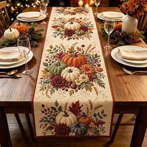 May include: A cream-colored quilted table runner featuring a repeating pattern of orange, white, and green pumpkins, autumn leaves, wheat stalks, and dark red flowers. The runner has a thin rust-colored border and a textured, stitched surface.