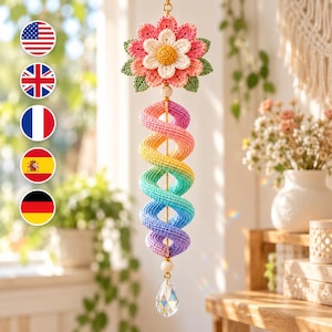 May include: A hanging crochet ornament featuring a multi-layered flower with pink, white, and green petals at the top, followed by a long, spiraling rainbow-colored crochet tail, finished with a clear, faceted crystal teardrop pendant.