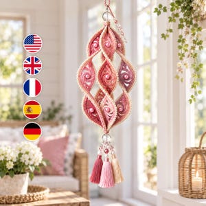 Peut inclure: Un ornement en spirale suspendu en fil crocheté dans des tons rose, pêche et bordeaux, agrémenté de perles, d'un cristal transparent au sommet et de trois pompons pendants aux couleurs rose foncé, rose clair et crème.