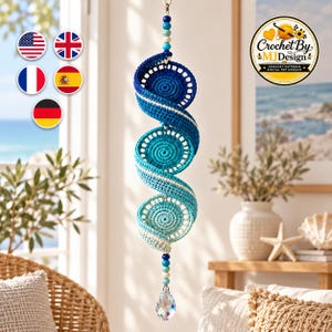 May include: A hanging crochet spiral ornament featuring a gradient of blue yarn, transitioning from dark navy to light turquoise. The spiral is accented with wooden beads at the top and bottom, ending with a clear, faceted crystal drop pendant.