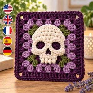 Könnte beinhalten: Ein quadratisches Häkelquadrat mit einem zentralen, cremeweißen Totenkopfmotiv, umgeben von violetten und hellvioletten Garnbüscheln sowie grünen blattartigen Akzenten. Der Rand ist in dunkelviolettem Garn gearbeitet und strukturiert.
