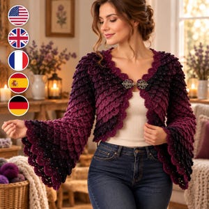 May include: A dark purple and black ombre crochet bolero jacket featuring a textured scale-like pattern, long flared sleeves, and a decorative silver-toned metal clasp closure at the center front, worn over a plain white top and blue jeans.