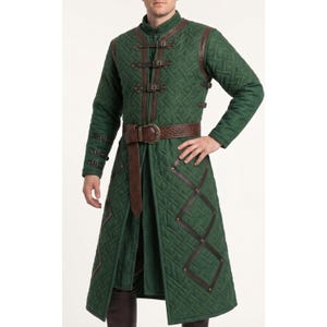 May include: A long, forest green quilted coat featuring a high collar, long sleeves, and a front closure with three brown leather straps and metal buckles. The coat includes brown leather trim, a matching wide belt, and additional buckle details on the sleeves.