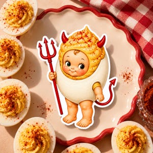 May include: A sticker featuring a baby character dressed as a deviled egg, wearing a yellow piped egg yolk hat with red horns, a white egg white body suit, and a red tail, while holding a red trident, surrounded by several deviled egg halves.
