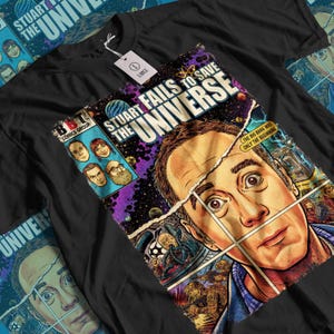 May include: A black t-shirt featuring a comic book style graphic print titled Stuart Fails to Save the Universe. The design includes a large portrait of a man, smaller character heads, space imagery, and the text The Big Bang Was Only the Beginning.