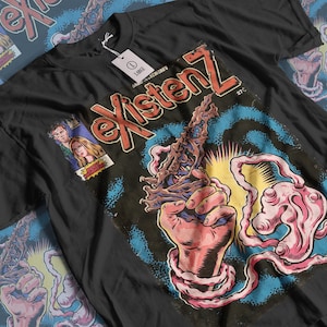 May include: A black t-shirt featuring a graphic print in the style of a comic book cover. The text reads "existenZ" in large red letters. The illustration depicts a hand holding a textured, organic-looking weapon with pink, flowing tendrils.