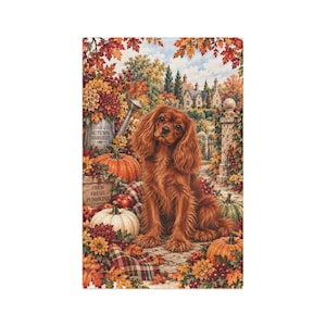 May include: A decorative tapestry featuring a brown Cavalier King Charles Spaniel sitting amidst an autumn harvest scene. The image includes orange and white pumpkins, colorful fall foliage, a metal bucket labeled Autumn Harvest, and a stone house.
