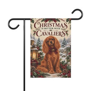 May include: A rectangular garden flag hanging on a black metal stand. The flag features a brown Cavalier King Charles Spaniel wearing a red bow with gold bells, surrounded by pine branches, pinecones, red berries, and a lantern. Text reads: CHRISTMAS IS BETTER WITH CAVALIERS.