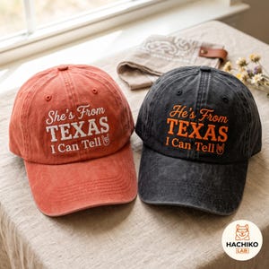 Può includere: Due cappellini da baseball, uno rosso sbiadito e uno grigio antracite, entrambi con testo ricamato. Il cappellino rosso riporta la scritta She's From TEXAS I Can Tell con un'icona di gesto. Il cappellino grigio riporta He's From TEXAS I Can Tell.