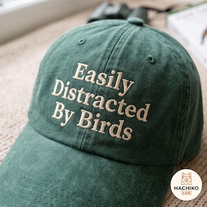 Op de afbeelding: Een bosgroene baseballpet met de geborduurde tekst "Easily Distracted By Birds" in lichtbeige draad. De pet heeft een gestructureerde kroon, een gebogen klep en gestikte oogjes op de bovenste panelen voor ventilatie en een klassieke pasvorm.