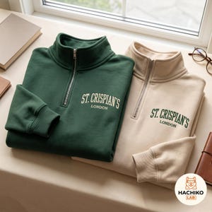 Puede incluir: Una sudadera verde oscuro con cremallera de cuarto y texto crema ST. CRISPIAN'S LONDON y una sudadera beige con cremallera de cuarto y texto verde oscuro ST. CRISPIAN'S LONDON. Ambas tienen cuello alto, cremallera plateada y puños acanalados.