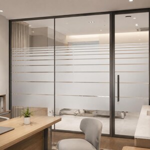Puede incluir: Un tabique de cristal de suelo a techo con marco de metal oscuro y lámina de privacidad esmerilada con franjas horizontales transparentes. La partición incluye una puerta de cristal abatible con tirador vertical que separa dos oficinas.