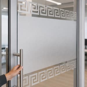 Op de afbeelding: Een glazen kantoordeur met een brede horizontale strook van gematteerde privacyfolie. De folie is aan de boven- en onderkant afgezet met een wit Grieks sleutelpatroon. Een verticale handgreep van geborsteld metaal zit aan het deurkozijn.