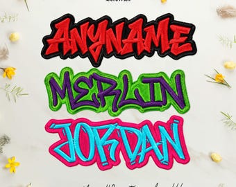 Puede incluir: Tres parches bordados con nombres en fuente estilo grafiti. El parche superior es rojo con borde negro y dice ANYNAME. El parche central es morado con borde verde y dice MERLIN. El parche inferior es azul con un borde de color rosa intenso.