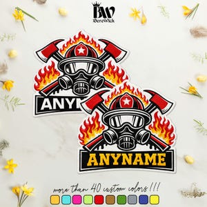 May include: Two identical die-cut stickers featuring a graphic of a firefighter helmet with a gas mask, crossed axes, and orange and yellow flames. Below the graphic is a black rectangular banner with the yellow text ANYNAME.