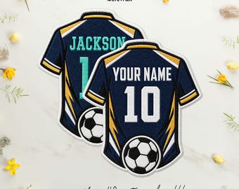 Puede incluir: Dos parches bordados de camisetas de fútbol en azul marino con detalles en amarillo y blanco. Un parche muestra el nombre JACKSON y el número 10 en turquesa, el otro muestra YOUR NAME y el número 10 en blanco. Ambos incluyen un gráfico de balón.