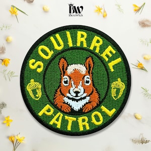 May include: A circular embroidered patch featuring a brown squirrel centered on a dark green background. The text SQUIRREL PATROL is stitched in yellow letters around the border, accompanied by two small yellow acorn icons on the sides.
