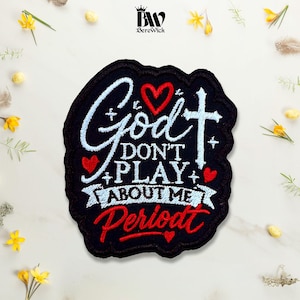 May include: A black embroidered patch featuring the white text "God DON'T PLAY ABOUT ME" and the red text "Periodt". The design includes a white cross, three red hearts, and small white star accents. The patch has a black stitched border.