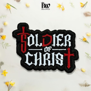 May include: A black embroidered patch featuring the white text Soldier of Christ. The letter S is stylized as a red sword, and a red cross is positioned at the end of the word Christ. The patch has a black border and a scalloped edge design.