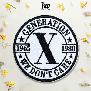May include: A circular embroidered patch featuring a white background with a thick black border. The text GENERATION X is arched at the top, with WE DON'T CARE at the bottom. A large black letter X sits in the center, flanked by 1965 and 1980.