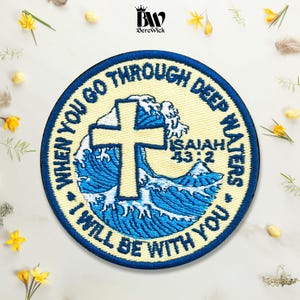 May include: A circular embroidered patch featuring a cream-colored background with a blue border. The design includes a central yellow cross over blue ocean waves, with the text "WHEN YOU GO THROUGH DEEP WATERS I WILL BE WITH YOU" and "ISAIAH 43:2".