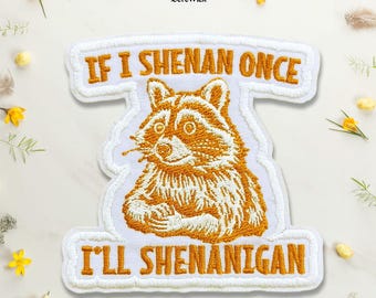 Puede incluir: Un parche bordado blanco con una ilustración de un mapache de color naranja dorado en el centro. El texto "IF I SHENAN ONCE" está bordado en naranja dorado sobre el mapache, y "I'LL SHENANIGAN" está bordado en naranja dorado debajo.