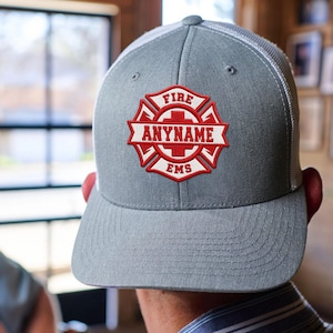 May include: A grey baseball cap with a white mesh back and a red and white embroidered patch on the front. The patch features a Maltese cross design with the text FIRE at the top, EMS at the bottom, and the word ANYNAME in the center banner.