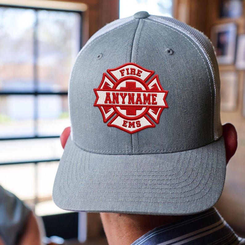 May include: A grey baseball cap with a white mesh back and a red and white embroidered patch on the front. The patch features a Maltese cross design with the text FIRE at the top, EMS at the bottom, and the word ANYNAME in the center banner.