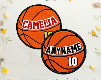 Puede incluir: Dos parches circulares bordados de baloncesto con bordes negros. El parche superior presenta el nombre CAMELIA en letras rojas con contornos blancos. El parche inferior muestra el texto ANYNAME en letras negras con contornos blancos y el número 10.