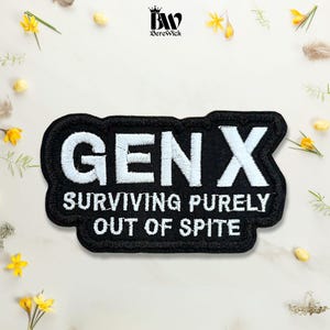 May include: A black rectangular embroidered patch with a scalloped edge featuring the white text GEN X SURVIVING PURELY OUT OF SPITE. The patch has a thick black border and is centered against a light background with scattered yellow flowers.