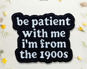 Puede incluir: Un parche bordado negro con borde festoneado que presenta el texto blanco cosido "be patient with me i'm from the 1900s" en una fuente negrita sin remates. El parche tiene una apariencia de tela texturizada y un mensaje legible.
