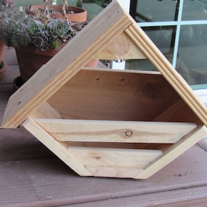 May include: A wooden birdhouse with a triangular roof and a small opening for birds to enter. The birdhouse is made of natural wood and has a rustic appearance.